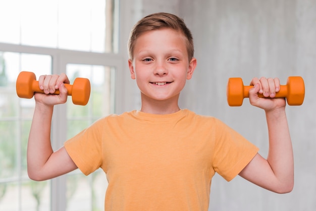 Retrato, de, um, sorrindo, homem jovem, segurando, dumbbell, em, mãos, olhando câmera