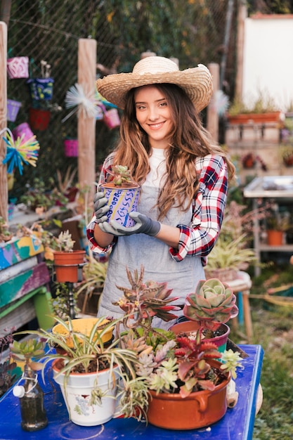 Retrato, de, um, sorrindo, jovem, femininas, jardineiro, desgastar, chapéu, segurando, pintado, planta panela, em, estufa