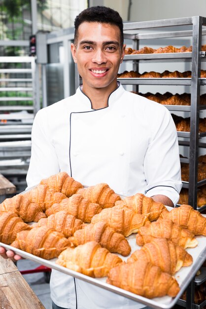 Retrato, de, um, sorrindo, macho, padeiro, segurando bandeja, de, croissant cozido