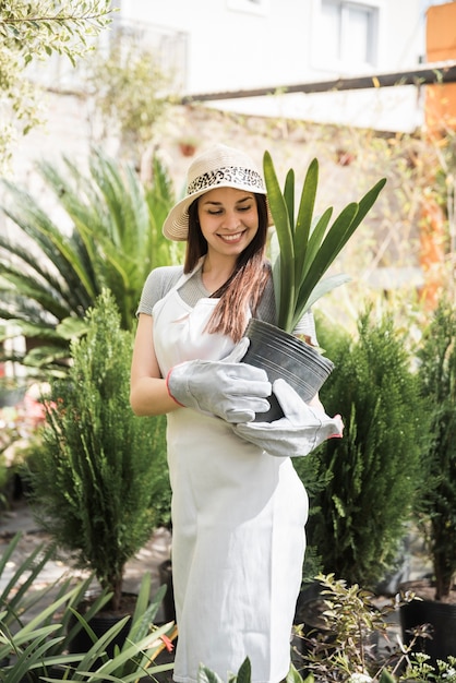 Foto grátis retrato, de, um, sorrindo, mulher jovem, olhar, planta pote, segure, em, dela, mãos