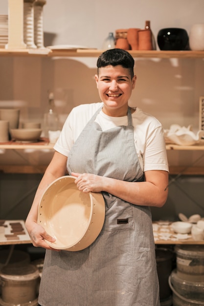 Foto grátis retrato, de, um, sorrindo, mulher jovem, segurando, cerâmico, recipiente, em, mão