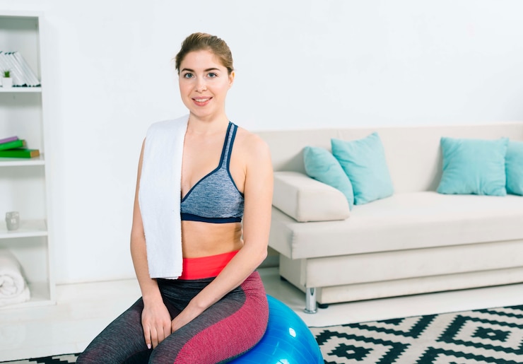 Foto grátis retrato, de, um, sorrindo, mulher jovem, sentando, ligado, pilates, bola, em, a, modernos, sala de estar