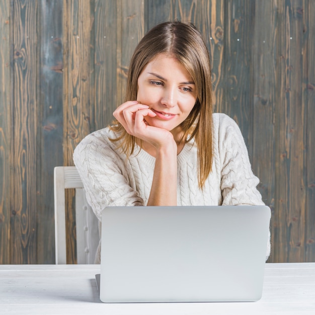 Foto grátis retrato, de, um, sorrindo, mulher jovem, usando computador portátil, escrivaninha