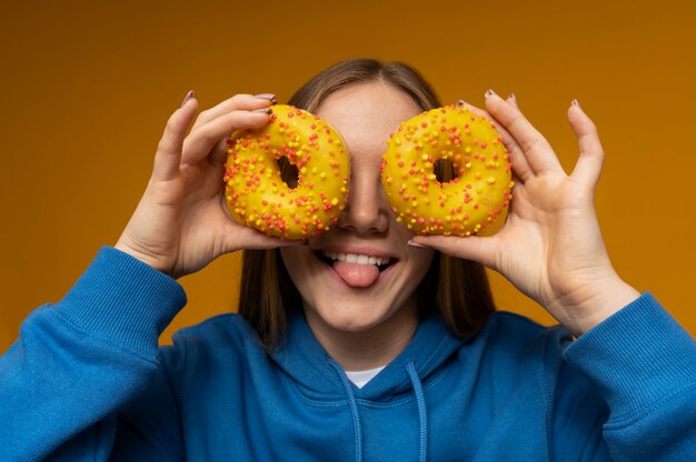 Retrato de uma adolescente com a língua para fora e usando dois donuts como copos