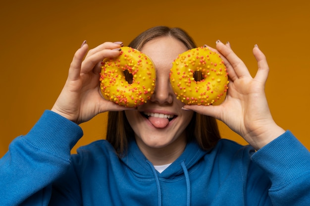 Retrato de uma adolescente com a língua para fora e usando dois donuts como copos