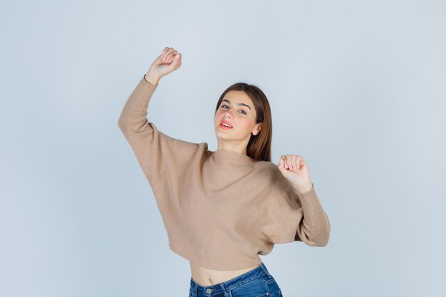 Retrato de uma adolescente mostrando um gesto de vencedor com um suéter, jeans e uma alegre vista frontal