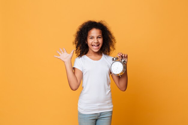 Retrato de uma alegre menina africana segurando o relógio despertador