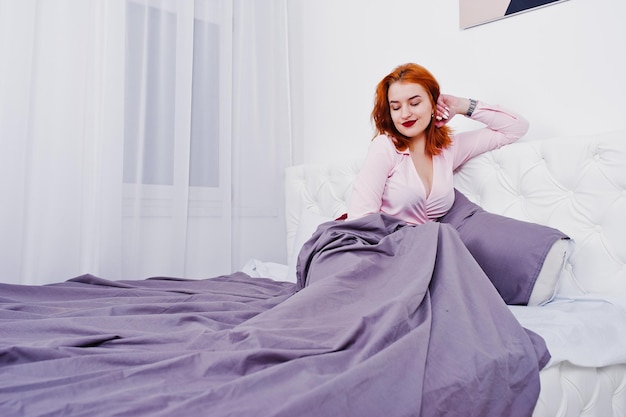 Retrato de uma atraente ruiva deitada na cama e cobrindo-se com um cobertor roxo