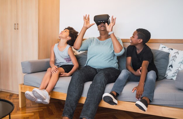 Retrato de uma avó afro-americana e netos brincando com óculos de Vr em casa. Conceito de família e tecnologia.