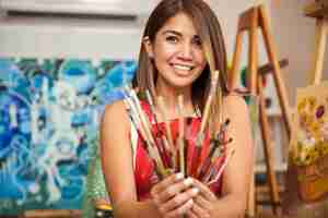 Foto grátis retrato de uma bela artista feminina segurando um monte de pincéis e sorrindo enquanto trabalhava em seu estúdio