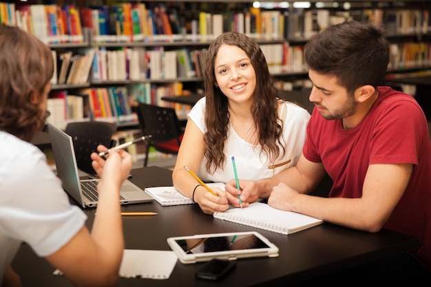 Retrato de uma bela estudante universitária sorrindo enquanto estudava com seus amigos na biblioteca