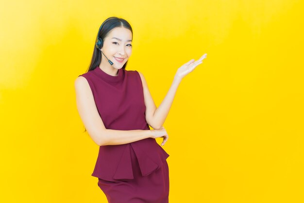 Retrato de uma bela jovem asiática com centro de atendimento ao cliente de call center na parede amarela amarela