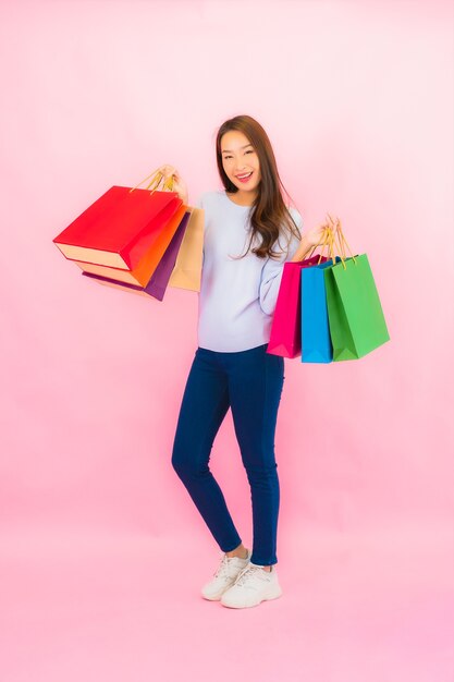 Retrato de uma bela jovem asiática com uma sacola de compras colorida em uma parede isolada de cor rosa.