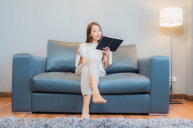 Retrato de uma bela jovem asiática lendo um livro no sofá no interior da sala de estar
