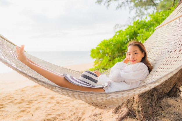 Retrato de uma bela jovem asiática relaxando em uma rede ao redor da praia nas férias