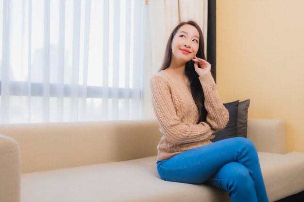 Retrato de uma bela jovem asiática relaxando um sorriso feliz no interior da decoração do sofá do quarto