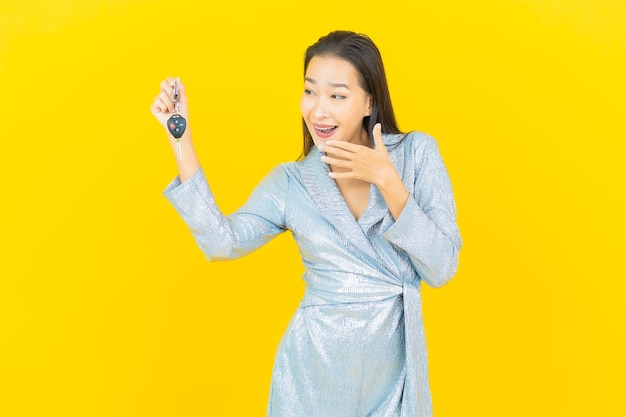 Retrato de uma bela jovem asiática sorrindo com a chave do carro na parede amarela