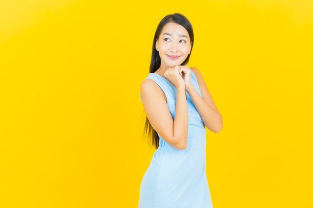 Retrato de uma bela jovem asiática sorrindo com ação na parede de cor amarela