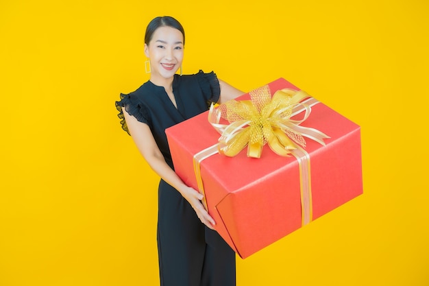 Retrato de uma bela jovem asiática sorrindo com caixa de presente vermelha em amarelo