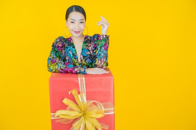 Retrato de uma bela jovem asiática sorrindo com caixa de presente vermelha em amarelo