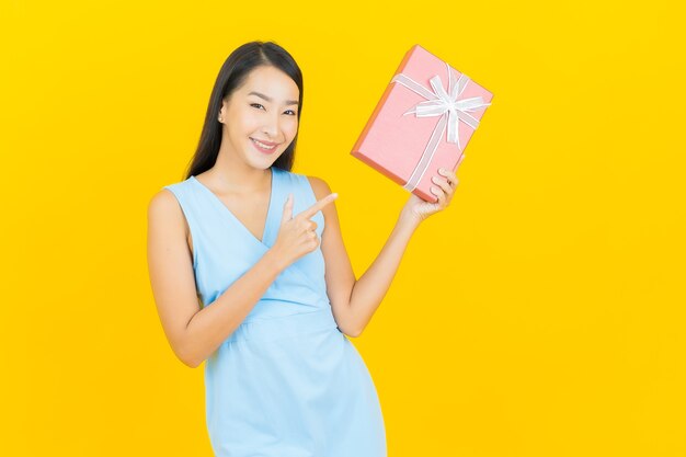 Retrato de uma bela jovem asiática sorrindo com caixa de presente vermelha na parede de cor amarela