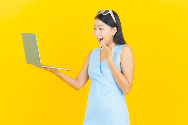 Retrato de uma bela jovem asiática sorrindo com computador laptop na parede amarela isolada