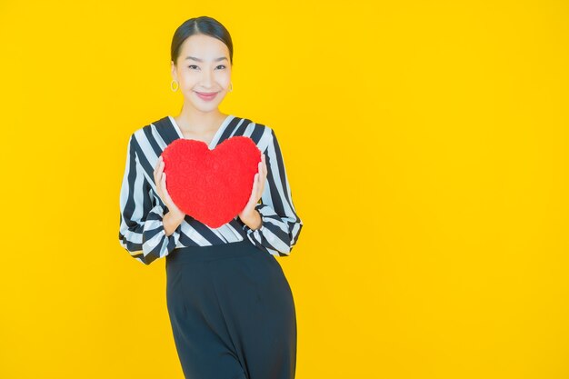 Retrato de uma bela jovem asiática sorrindo com forma de almofada de coração amarelo