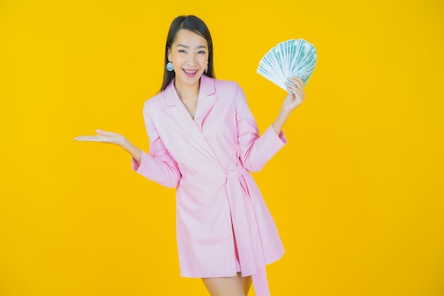 Retrato de uma bela jovem asiática sorrindo com muito dinheiro e dinheiro na cor de fundo
