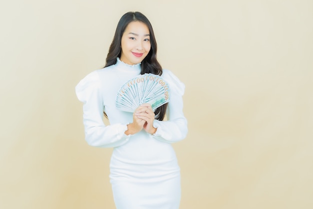 Retrato de uma bela jovem asiática sorrindo com muito dinheiro e dinheiro na parede colorida