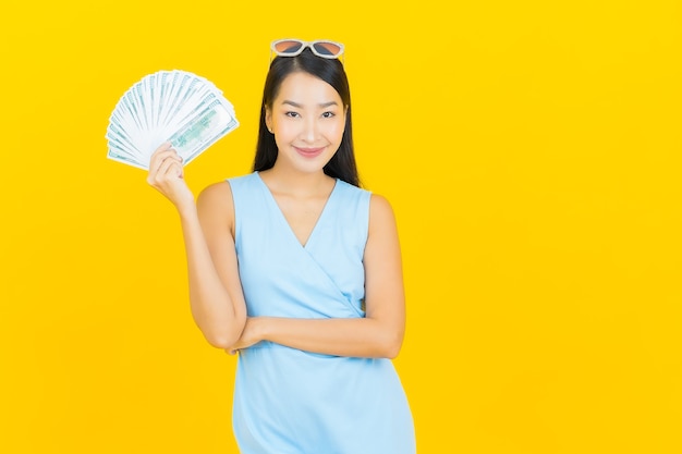 Retrato de uma bela jovem asiática sorrindo com muito dinheiro e dinheiro na parede de cor amarela