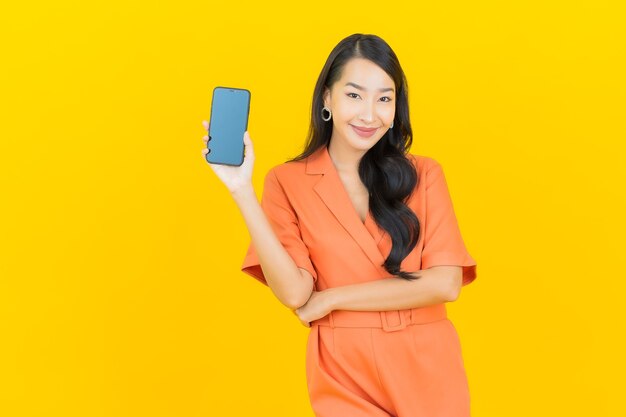 Retrato de uma bela jovem asiática sorrindo com um celular inteligente em amarelo