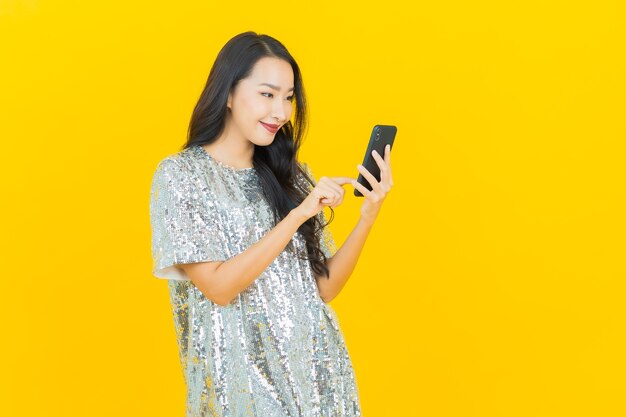 Retrato de uma bela jovem asiática sorrindo com um celular inteligente em amarelo