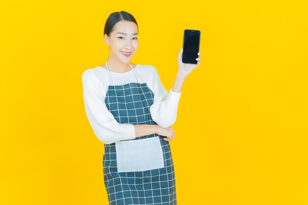 Foto grátis retrato de uma bela jovem asiática sorrindo com um celular inteligente em amarelo