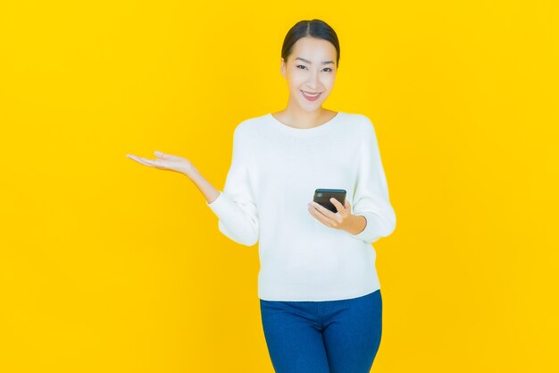 Retrato de uma bela jovem asiática sorrindo com um celular inteligente em amarelo