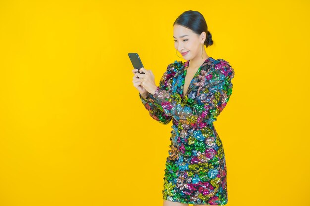 Retrato de uma bela jovem asiática sorrindo com um celular inteligente em amarelo