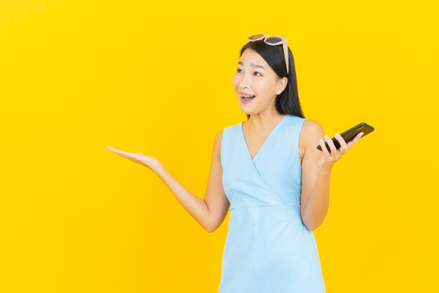 Retrato de uma bela jovem asiática sorrindo com um celular inteligente na parede amarela