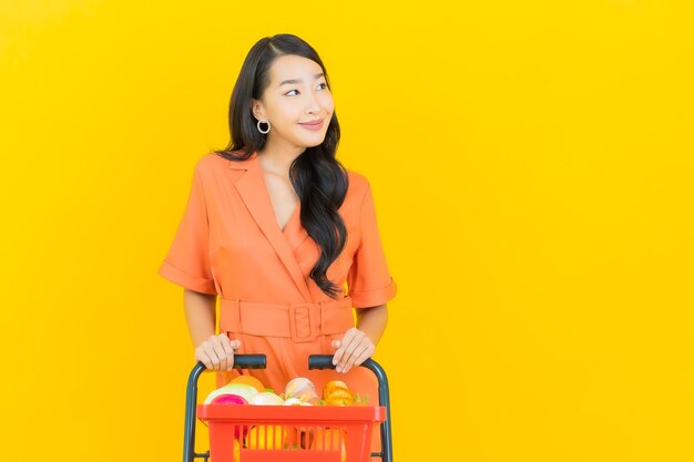 Retrato de uma bela jovem asiática sorrindo com uma cesta de supermercado em amarelo