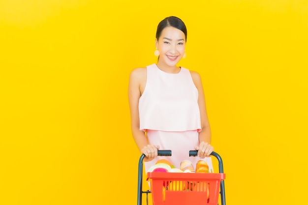 Retrato de uma bela jovem asiática sorrindo com uma cesta de supermercado em amarelo