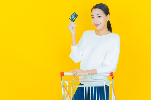 Retrato de uma bela jovem asiática sorrindo com uma cesta de supermercado em amarelo