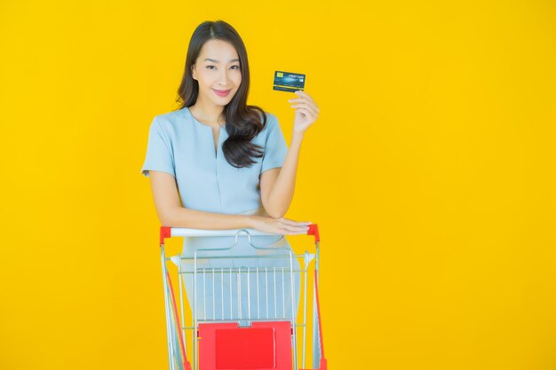 Retrato de uma bela jovem asiática sorrindo com uma cesta de supermercado na cor de fundo.