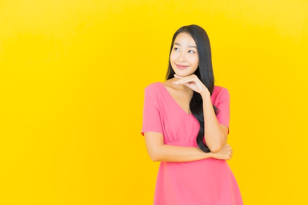 Retrato de uma bela jovem asiática sorrindo em um vestido rosa na parede amarela