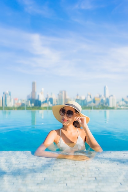 Retrato de uma bela jovem asiática sorrir relaxar o lazer ao redor da piscina ao ar livre com vista para a cidade