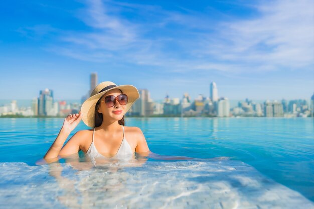 Retrato de uma bela jovem asiática sorrir relaxar o lazer ao redor da piscina ao ar livre com vista para a cidade
