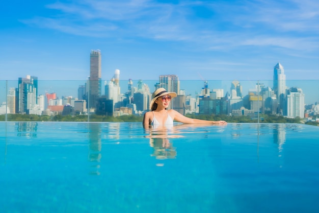 Retrato de uma bela jovem asiática sorrir relaxar o lazer ao redor da piscina ao ar livre com vista para a cidade