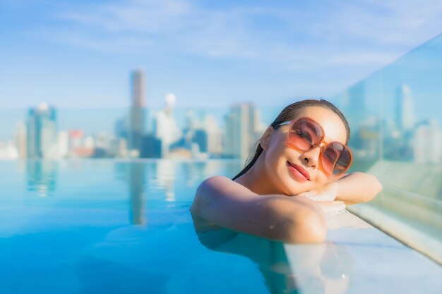 Retrato de uma bela jovem asiática sorrir relaxar o lazer ao redor da piscina ao ar livre com vista para a cidade