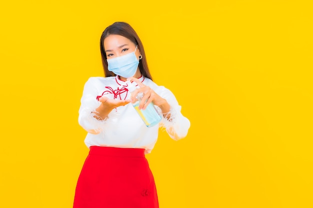 Retrato de uma bela jovem asiática usa máscara e usa álcool gel para proteger covid19 em amarelo