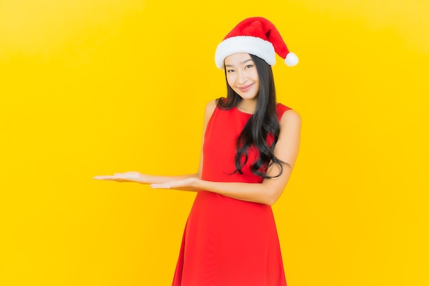 Retrato de uma bela jovem asiática usando chapéu de Papai Noel ou faixa para cabelo na parede amarela