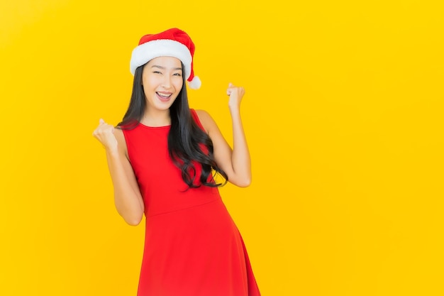 Retrato de uma bela jovem asiática usando chapéu de Papai Noel ou faixa para cabelo na parede amarela