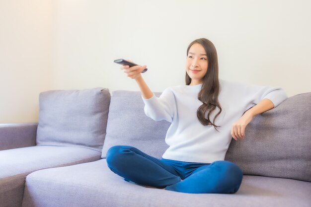 Retrato de uma bela jovem asiática usando controle remoto para mudar de canal na televisão