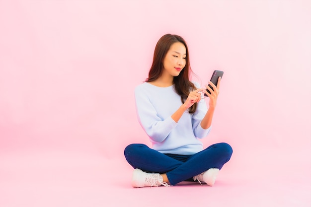 Retrato de uma bela jovem asiática usando telefone celular inteligente na parede isolada de cor rosa